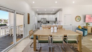 Une cuisine moderne avec des meubles blancs, un réfrigérateur en acier inoxydable et un coin repas comprenant une table en bois et des chaises en osier.
