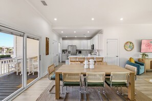 A modern kitchen with white cabinets, a stainless steel refrigerator, and a dining area with a wooden table and wicker chairs. - Palm Paradise - Heated pool & Hot tub + Golf Cart (North Myrtle Beach)