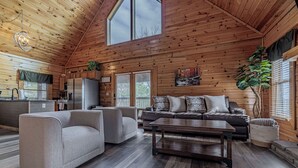 A spacious living area with a high ceiling, wooden walls, a large window, and a modern kitchen. - Enchanted Eagle cabin, 3 bedroom, with Hot tub and games room (Sevierville)