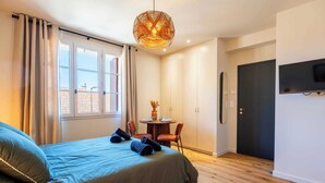 Quarto com cama, mesa redonda com cadeiras, TV fixada na parede e uma porta.