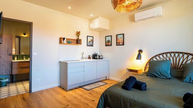 Quarto com cama, mesa de cabeceira, luminária e ar condicionado fixado na parede.
