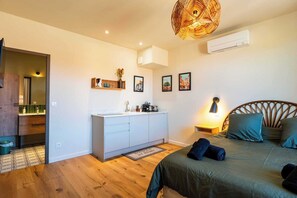 Quarto com cama, mesa de cabeceira, luminária e ar condicionado fixado na parede.