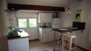 A compact kitchen with white cabinets, a countertop, a refrigerator, and two stools.