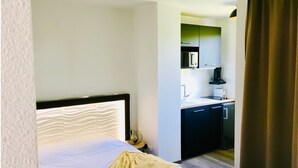 A hotel room with a bed, a small kitchenette, and a bathroom. - Elegant studio with balcony 5 min from Honfleur parking and swimming pool (Équemauville)