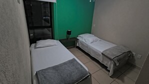 Ein kleiner, sauberer Raum mit zwei Betten, einem Deckenventilator und einer grünen Wand.