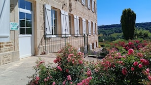Un bâtiment en pierre avec des volets blancs et une enseigne indiquant l’entrée pour les clients.