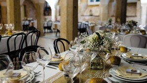 A restaurant with tables set for dining, featuring white tablecloths, wine glasses, and a centerpiece with flowers.