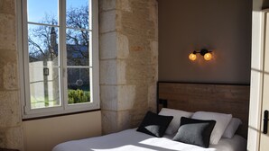 A bedroom with a large window, stone wall, wooden headboard, and two wall-mounted lights.