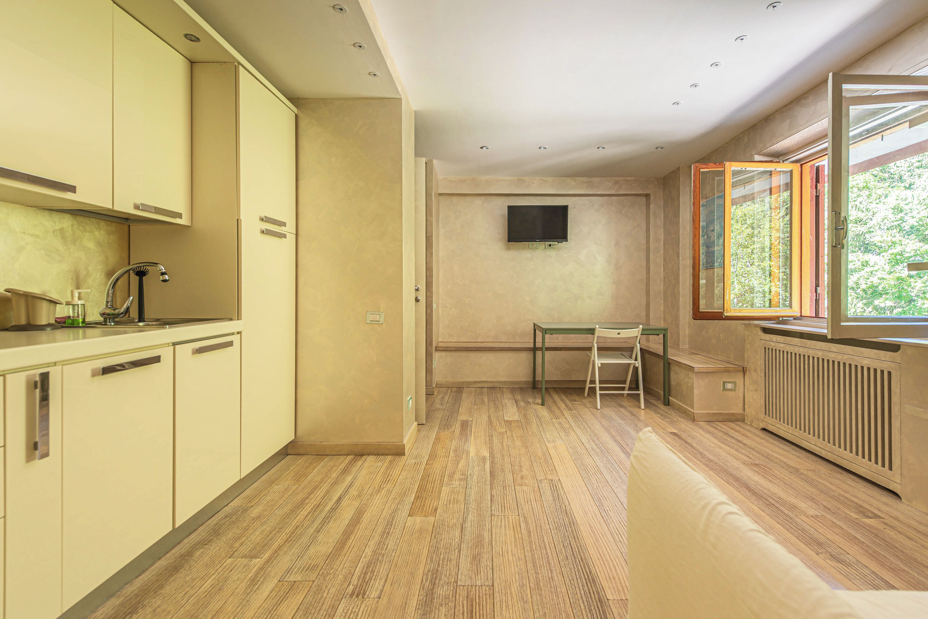 Una cocina moderna con comedor, televisor montado en la pared y ventana con vista a áreas verdes.