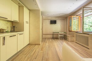 A modern kitchen with a dining area, a television mounted on the wall, and a window with a view of greenery. - La Casina (Pian De' Valli)