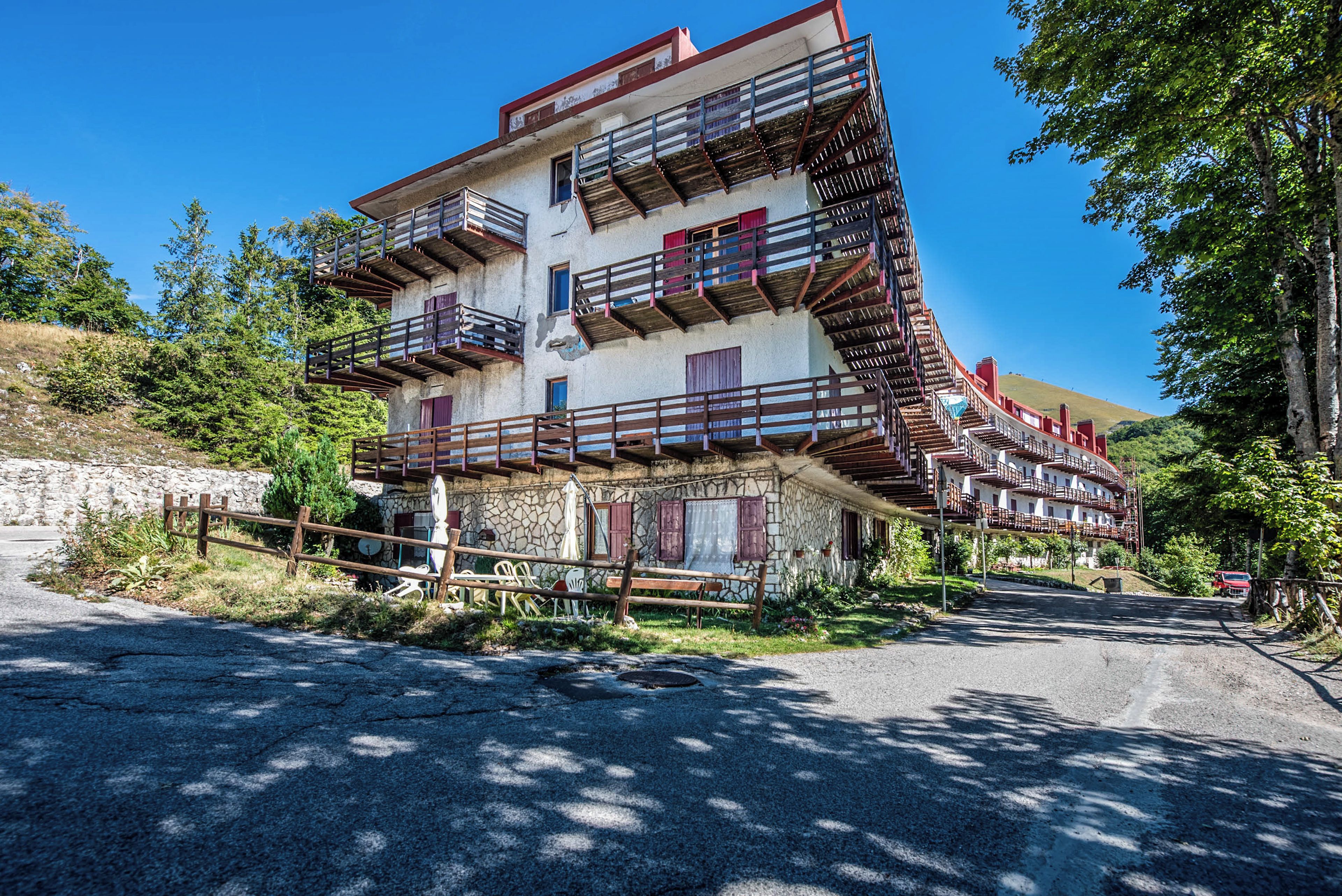 A multi-story building with balconies, a stone facade, and a surrounding natural landscape.