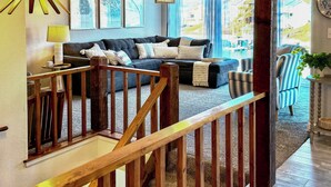 A modern living room with a dark-colored sectional sofa, a wooden staircase, and large windows offering a view of the outdoors. - Lake Views, Resort Perks! Osage Beach Retreat (Osage Beach)