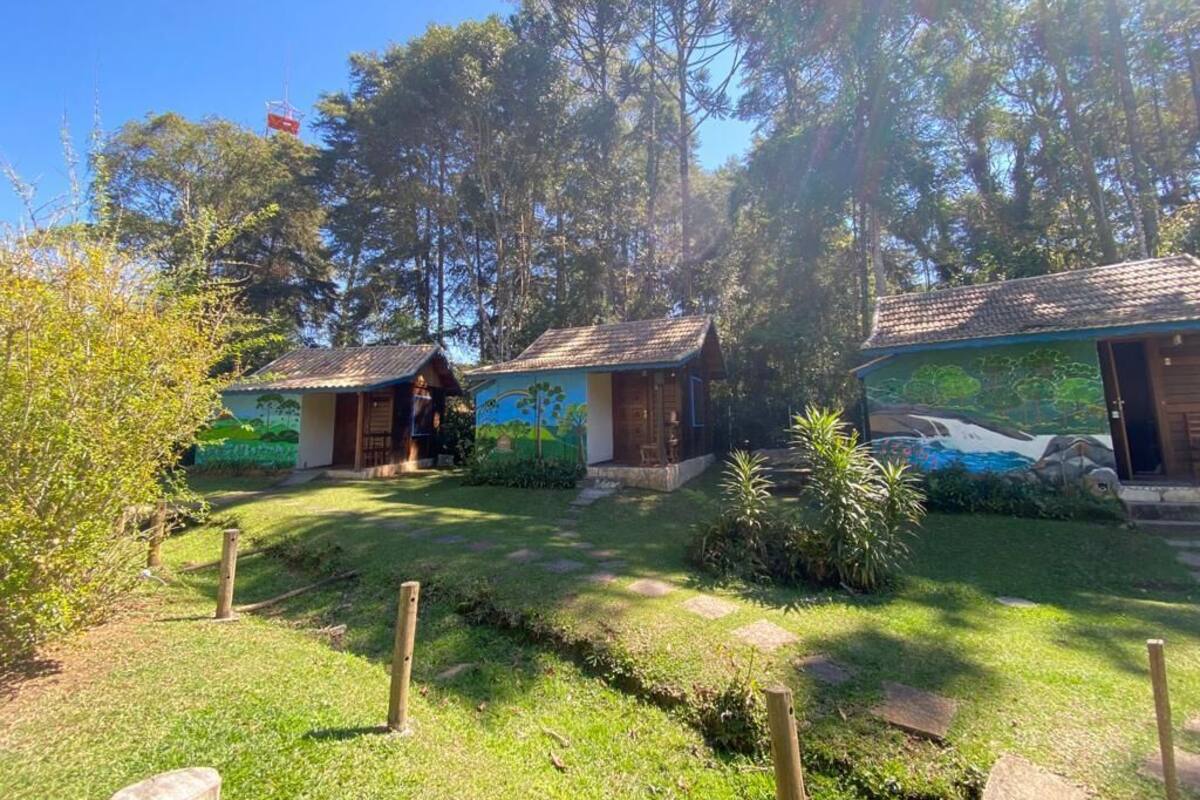 Un chalet rustique à toit de chaume, entouré d’une végétation luxuriante et surplombé d’un ciel bleu azur.