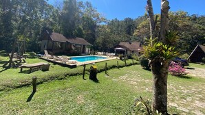 A backyard with a swimming pool, lounge chairs, and a small house. - Cabanas Do Visconde (Itatiaia)