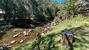 A natural outdoor setting with a stream, rocks, and dense greenery. - Cabanas Do Visconde (Itatiaia)