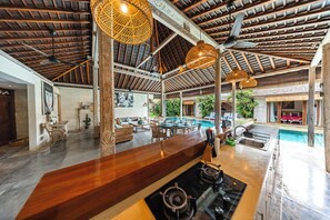 A spacious kitchen with a bar area, a pool, and a dining area with outdoor seating. - Stylish 4BR Canggu Villa • Private Pool & Sundeck • 8 Min to Beach (Badung Regency)