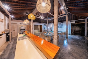 A spacious kitchen with a long wooden counter, hanging wicker light fixtures, and a high ceiling with exposed beams. - Stylish 4BR Canggu Villa • Private Pool & Sundeck • 8 Min to Beach (Badung Regency)
