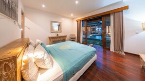 A bedroom with a bed, a wooden dresser, a desk, a chair, and a large window with curtains. - Stylish 4BR Canggu Villa • Private Pool & Sundeck • 8 Min to Beach (Badung Regency)