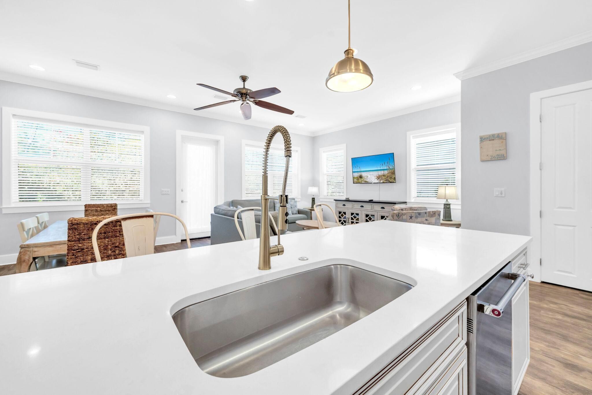 A modern kitchen with a large island, stainless steel sink, and a ceiling fan.