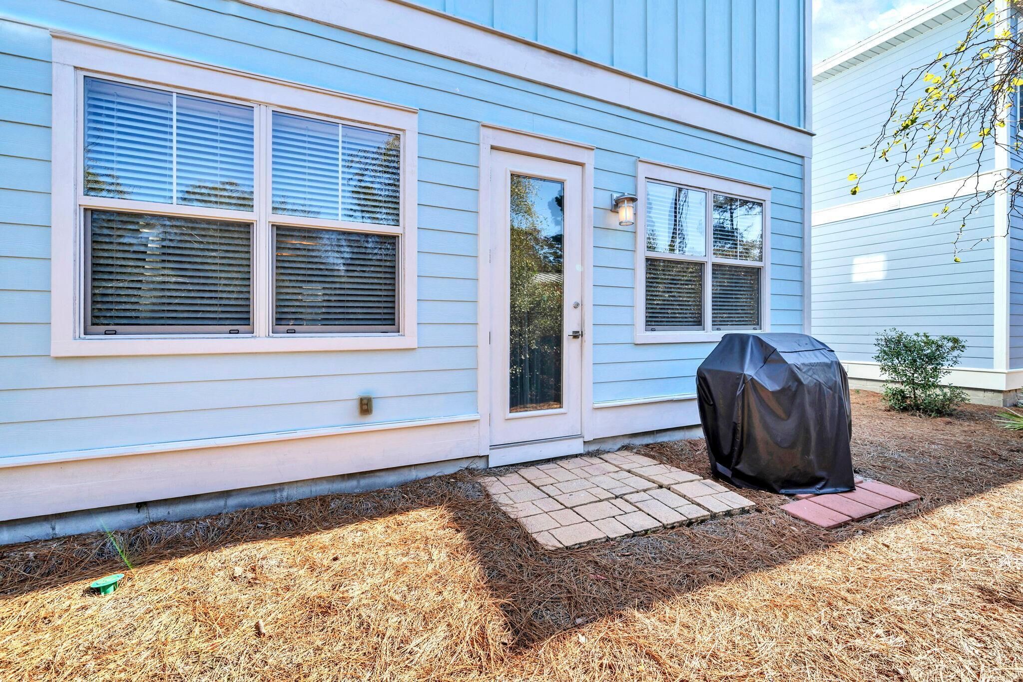 Une maison à l’extérieur bleu clair, avec une porte d’entrée et un barbecue couvert dans la cour.