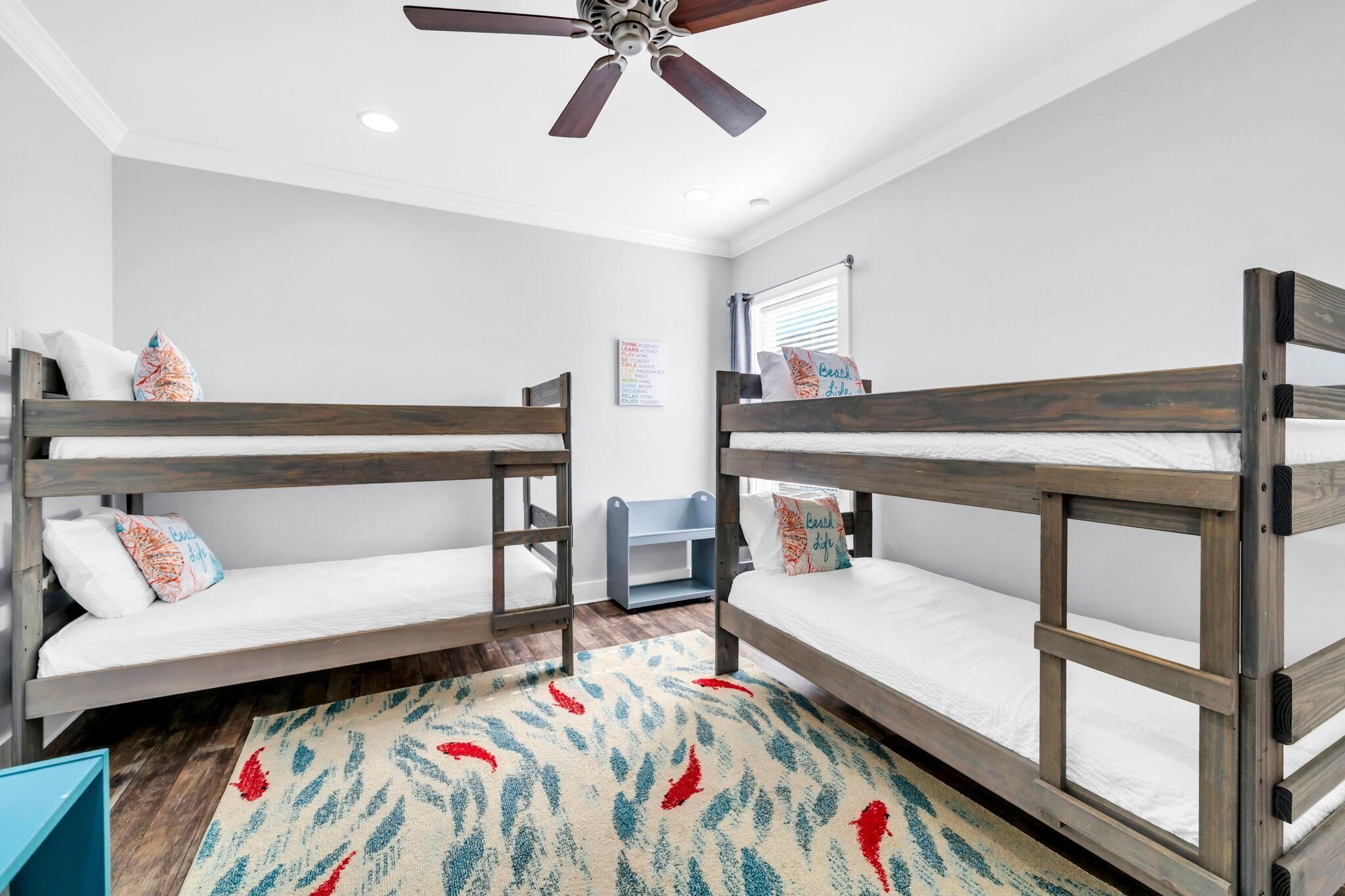 Huoneessa on kerrossängyt, kattotuuletin, ikkunassa sälekaihtimet ja lattialla lehtikuviollinen matto.