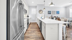 A modern kitchen with stainless steel appliances, a white countertop, and a wooden floor. - Shore Beats Work 30A (Santa Rosa Beach)