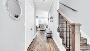 A hallway with a wooden floor, a staircase with a wooden handrail, and a mirror on the wall. - Shore Beats Work 30A (Santa Rosa Beach)