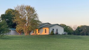 A single-story house with a green roof, a large tree in front, and a grassy yard. - Cozy 1-bedroom ranch house in Georgetown on 10 acres with horse paddock. (Georgetown)