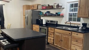 A modern kitchen with wooden cabinets, a stainless steel refrigerator, a black countertop, and a built-in oven. - Cozy 1-bedroom ranch house in Georgetown on 10 acres with horse paddock. (Georgetown)