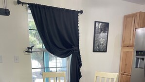 A dining area with a round table, four chairs, a window with curtains, a refrigerator, and a wall-mounted picture. - Cozy 1-bedroom ranch house in Georgetown on 10 acres with horse paddock. (Georgetown)