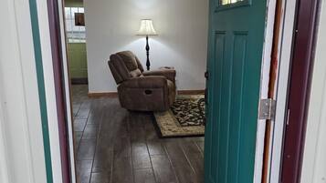Een kamer met een blauwgroene deur, een bruine stoel, een lamp en een kamerbreed tapijt met een patroon.