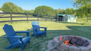 A grassy outdoor area with a fire pit and two Adirondack chairs. - Cozy 1-bedroom ranch house in Georgetown on 10 acres with horse paddock. (Georgetown)