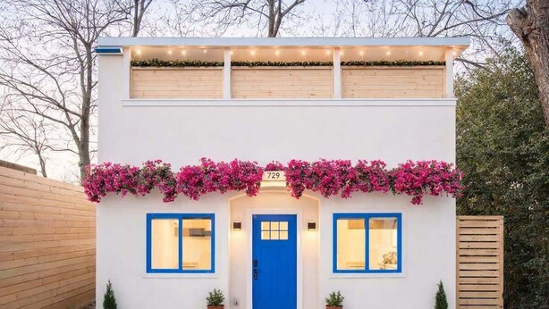Un edificio de dos pisos con una puerta azul, número 729, y un balcón con flores rosas.