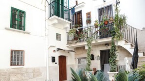 Ein Innenhof mit einem weißen Gebäude, einer Holztür und einer Treppe, die zu einem Balkon mit Blumentöpfen führt.