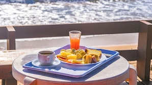 Un plateau de petit-déjeuner avec des toasts, des fruits et une tasse de café, posé sur une table offrant une vue sur l’océan.