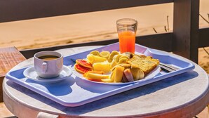 Un plateau de petit-déjeuner avec des toasts, des fruits et du jus, posé sur une table près de la plage.
