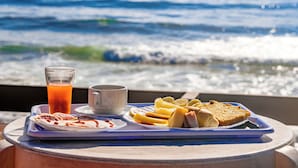 Un plateau contenant des aliments pour le petit-déjeuner, notamment des toasts, des fruits et un verre de jus d’orange, est disposé devant une vue sur l’océan.