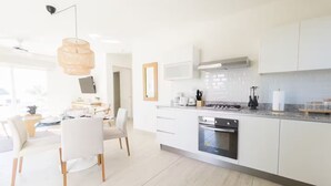 A modern kitchen with white cabinetry, a built-in oven, and a dining area with white chairs and a table. - Ocean Splendor Villa -C15-PBB-2 bed, 2 bath (Punta Chame)