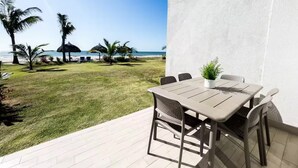A patio with a table and chairs, overlooking a beach with palm trees and a clear sky. - Ocean Splendor Villa -C15-PBB-2 bed, 2 bath (Punta Chame)