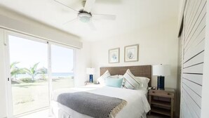 A bedroom with a bed, a nightstand, a ceiling fan, and a view of the beach. - Ocean Splendor Villa -C15-PBB-2 bed, 2 bath (Punta Chame)