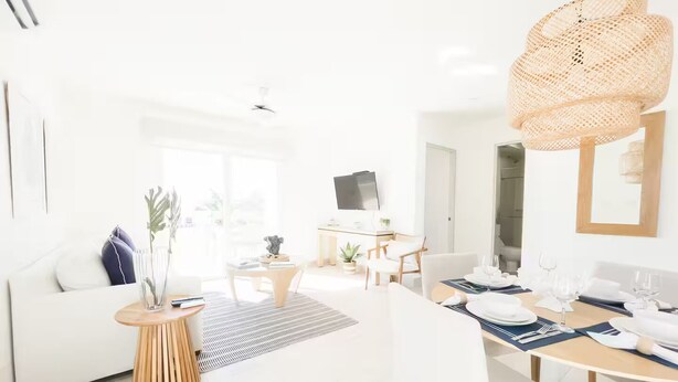 A bright, modern living room with a white sofa, a dining table set for a meal, and a large woven light fixture. - Ocean Splendor Villa -C15-PBB-2 bed, 2 bath (Punta Chame)
