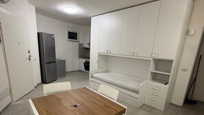 Ett kompakt kök med vita skåp, ett kylskåp, en mikrovågsugn och ett matbord med stolar.