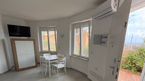Ett rymligt rum med ett matbord, stolar, en tv som är monterad på en träram och en dörr som leder ut till ett utomhusområde.