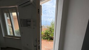 En öppen dörr som leder ut till en balkong med utsikt över en tegelvägg och grönska.
