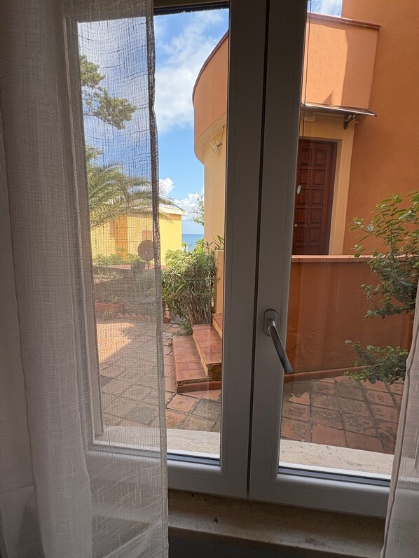 Blick durch ein Fenster mit einer Tür, einem Balkon und einem Gebäude mit einer gewölbten Fassade.