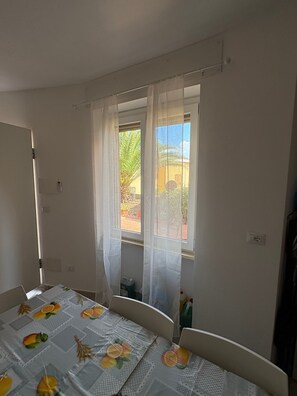 Ein Schlafzimmer mit Bett, Fenster mit durchsichtigen Vorhängen und Blick ins Freie.