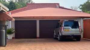 Un garage avec un toit rouge, un VUS garé et une plante en pot.