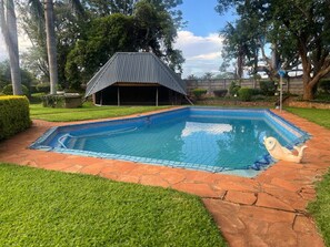 A swimming pool with a tiled edge, surrounded by a stone pathway and grass.