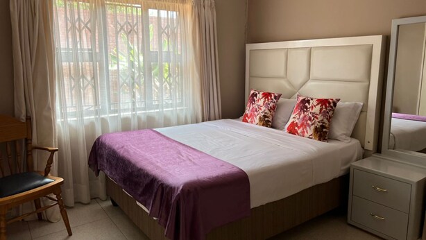 Une chambre bien rangée, avec un lit, une chaise, une table de chevet et une fenêtre avec des rideaux.