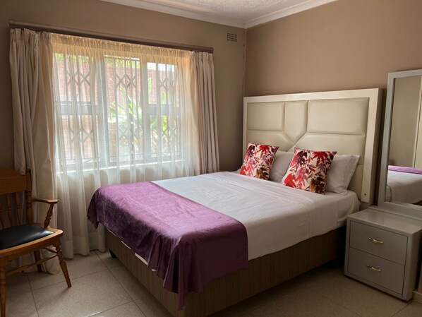 A neatly arranged bedroom with a bed, a chair, a nightstand, and a window with curtains.